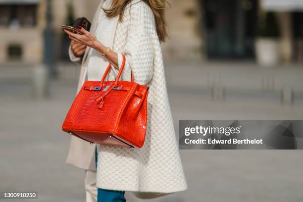 Passerby wears a white knitted long jacket, an orange leather crocodile pattern Hermes Birkin bag, a golden bracelet, blue jeans, on February 06,...