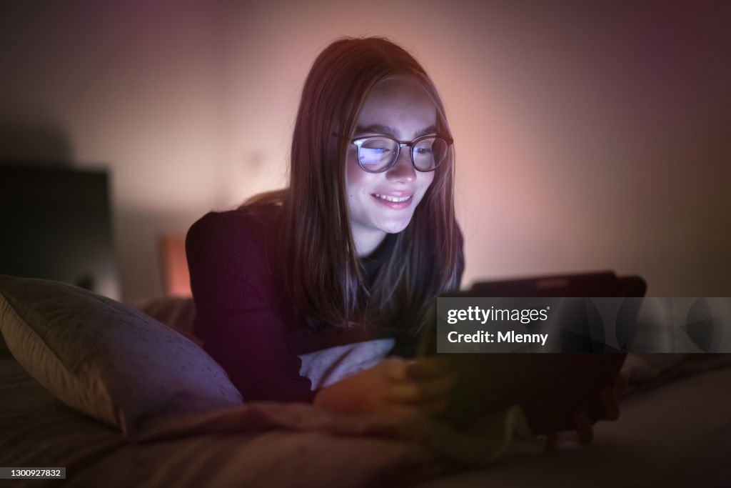 Smiling Teenage Woman lying in Bed using her Digital Tablet Computer