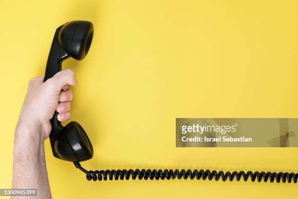 close up of a man's hand holding the intercom of an old black phone on a yellow background - telefonlur bildbanksfoton och bilder