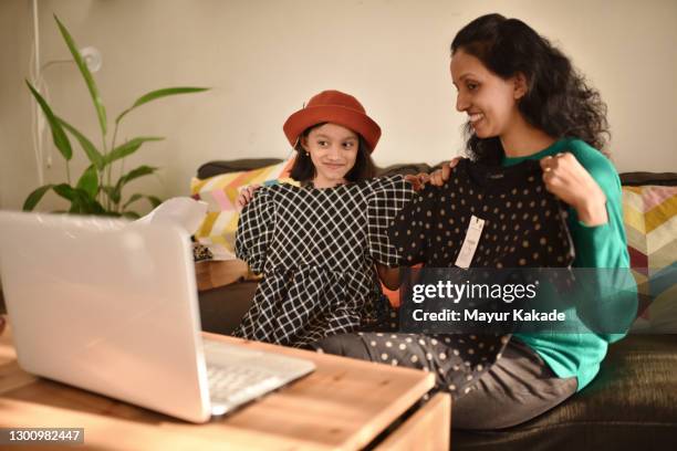 mother and daughter showing their new clothes through a video call using laptop - child delivering stock-fotos und bilder