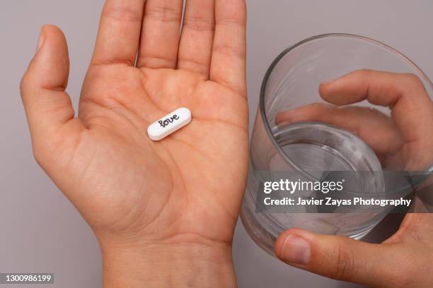 hands holding pill with text "love" and a glass of water - handfläche stock-fotos und bilder