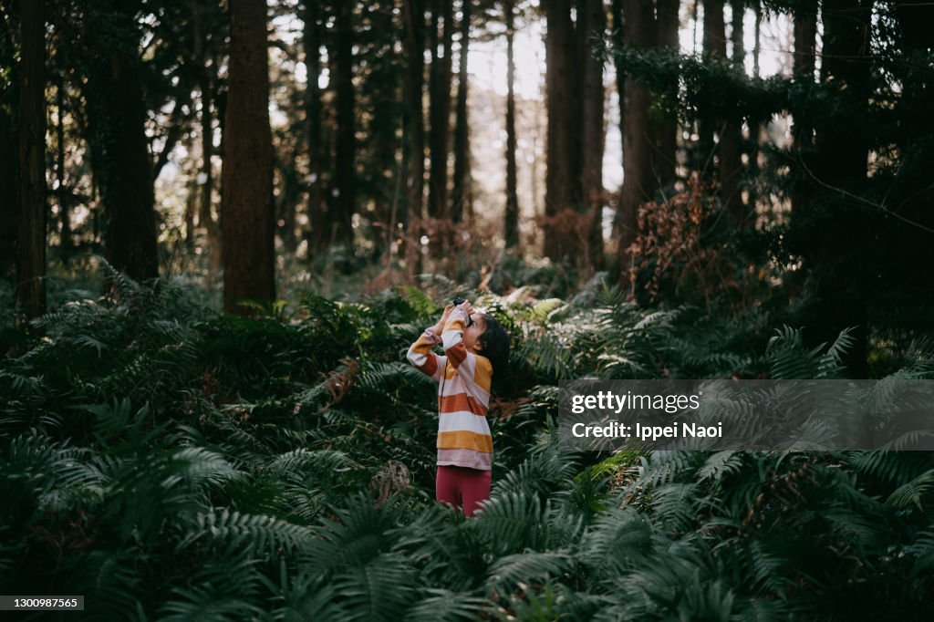 Young girl looking through binoculars in forest in winter