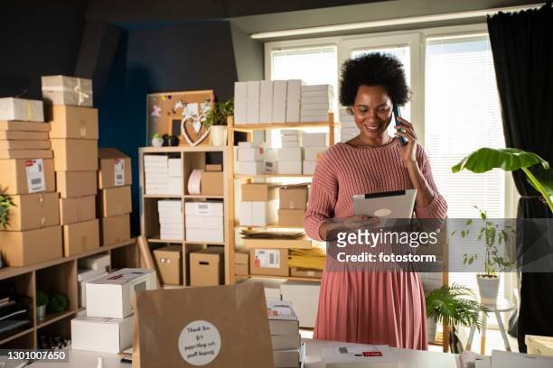 sonriente mujer dueña de un negocio usando tableta digital y hablando por teléfono - comercio electrónico fotografías e imágenes de stock
