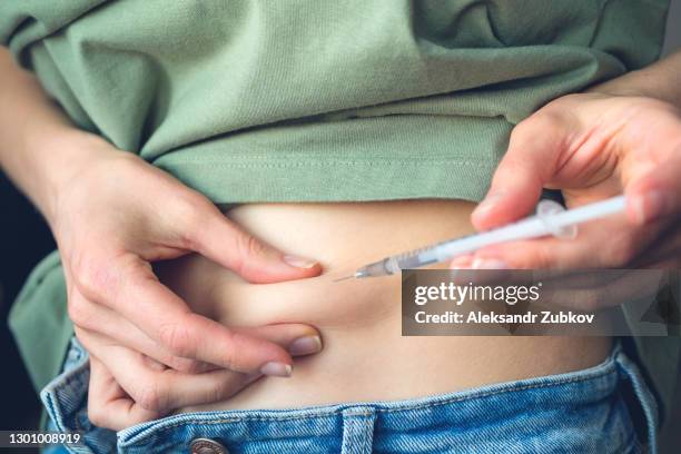 a woman with diabetes pulls back the skin on her stomach and gives an injection of insulin with a disposable syringe with a small needle, or a girl planning a pregnancy stimulates ovulation before artificial insemination or conception. - anticoagulant stock-fotos und bilder