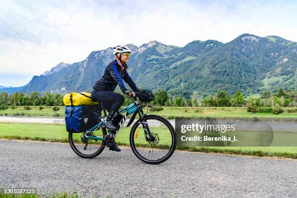 radfahrerin fährt fahrrad mit dem fahrrad entlang des flusses und der berge. - single lane road stock-fotos und bilder
