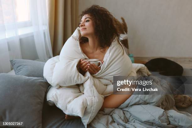 relaxed young woman drinking coffee in bed and looking in window - blanket bildbanksfoton och bilder