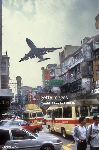 Scène de rue, circulation urbaine et avion de ligne au dessus des habitations Hong-Kong.