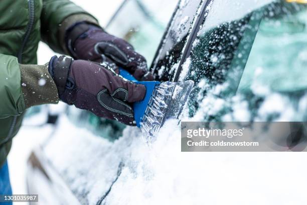 adult man de-icing snow covered car in winter - de ices stock pictures, royalty-free photos & images