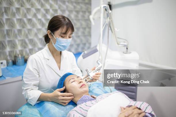 asian chinese women getting laser face treatment in a medical center, skin rejuvenation concept. cosmetic surgeon doctor giving fractional co2 laser skin treatment to a female patient. - beauty laser stock pictures, royalty-free photos & images