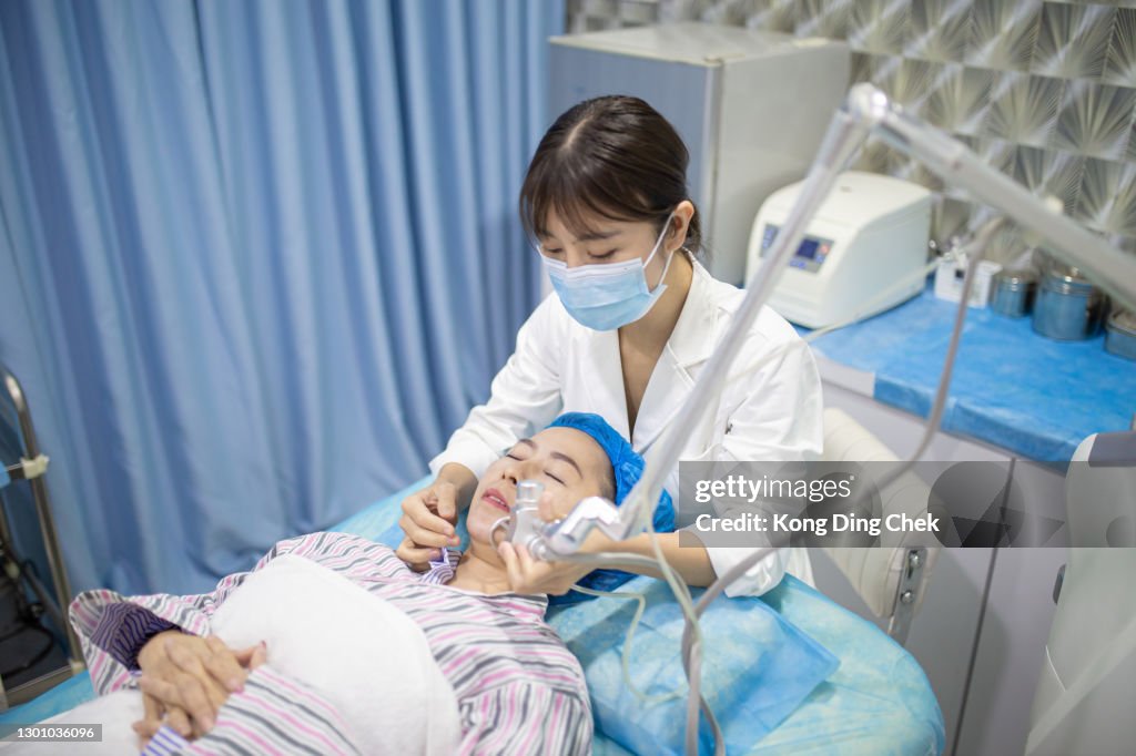 Las mujeres chinas asiáticas reciben tratamiento facial con láser en un centro médico, concepto de rejuvenecimiento de la piel. Médico cirujano cosmético que da tratamiento fraccional de la piel con láser de CO2 a una paciente femenina.
