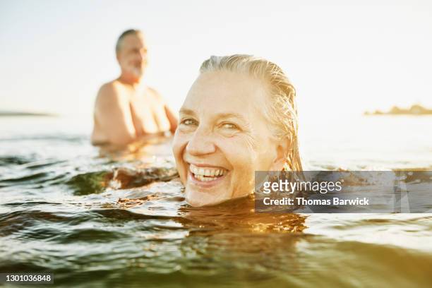 smiling senior woman swimming with friend in bay on summer evening - active lifestyle stock pictures, royalty-free photos & images