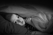 black and white portrait boy in bed with his eyes open. the child is afraid of ghosts. tormented by nightmares and terrible dreams in children