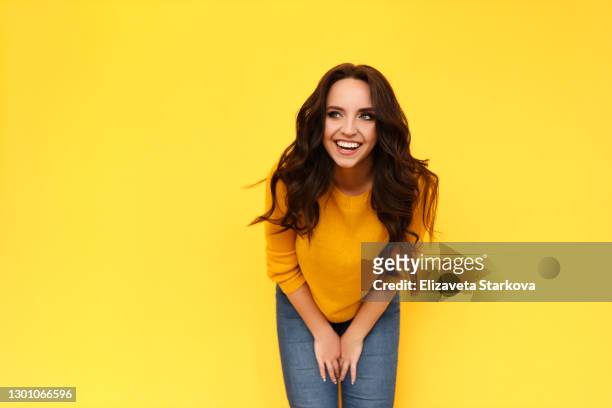 beautiful cheerful emotional laughing smiling curly-haired brunette woman in orange sweater having fun and looking away on bright yellow isolated background - surprised happy woman stock pictures, royalty-free photos & images