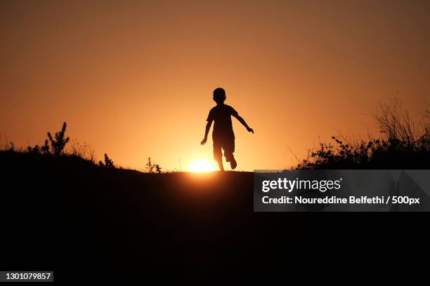 silhouette of boy running on field against sky during sunset,mila,algeria - algeria stockfoto's en -beelden