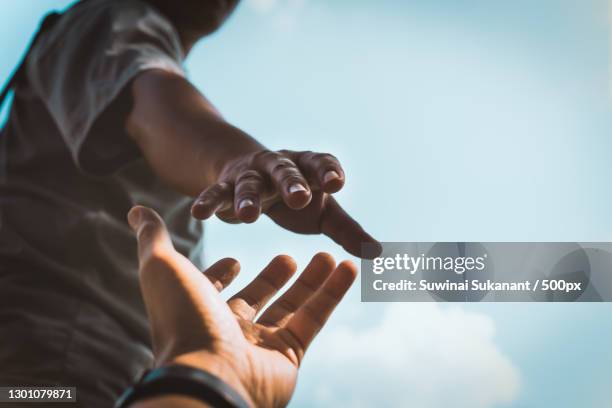 cropped hands reaching out to help each other against sky,thailand - apoyar fotografías e imágenes de stock