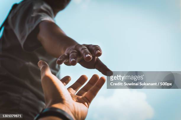 cropped hands reaching out to help each other against sky,thailand - sostegno morale foto e immagini stock