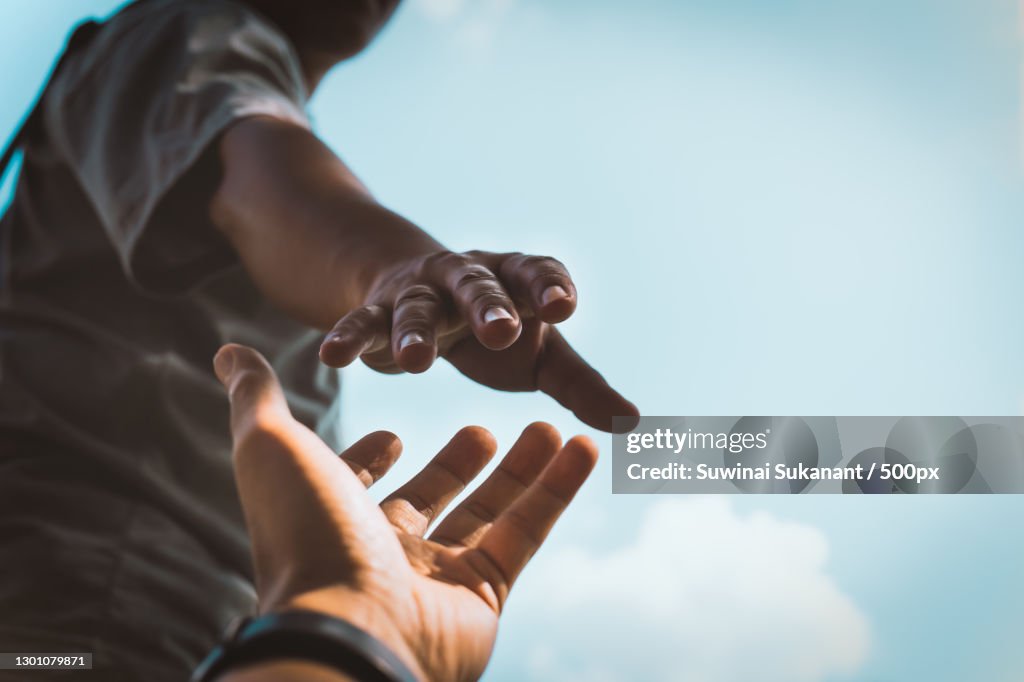 Cropped hands reaching out to help each other against sky,Thailand