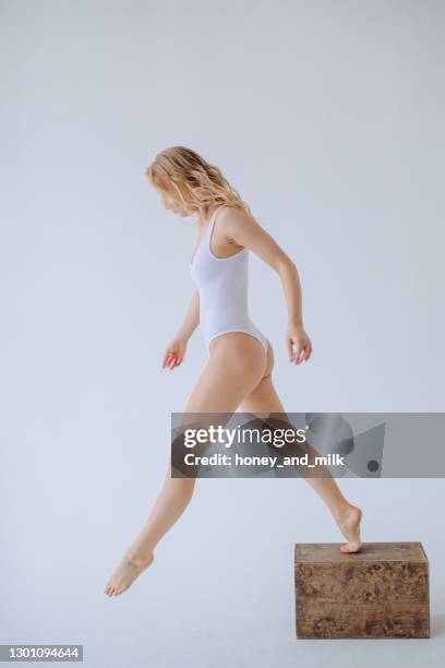 female gymnast in a white leotard stepping down off a wooden block - body foto e immagini stock