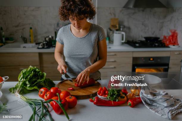 making a healthy and nutritious lunch: a young woman chopping vegetables in the kitchen - plant based diet stock pictures, royalty-free photos & images