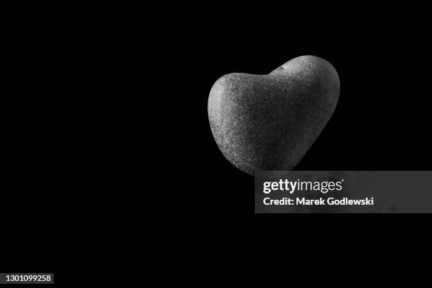 a heart-shaped stone in the air, black background, black and white - stone hand stock-fotos und bilder