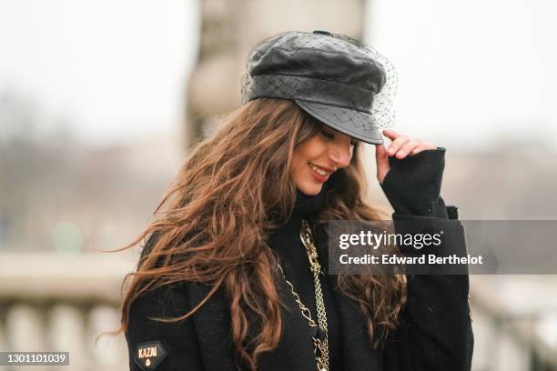 Carina Zavline wears a black leather beret hat with a veil from Dior, a black wool turtleneck pullover from Nu-In Fashion, a golden long chain...