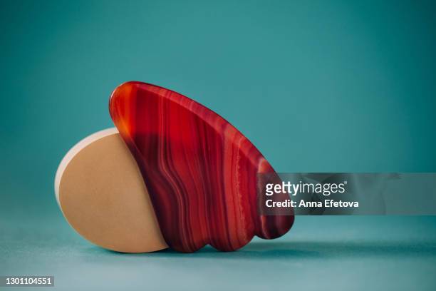 face massager guasha made of carnelian nearby beige circle shape podium on turquoise background. health and wellbeing concept - jade gemstone stockfoto's en -beelden
