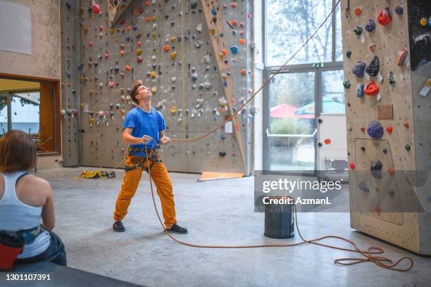 young male belayer looking up at indoor climbing wall - belaying stock pictures, royalty-free photos & images