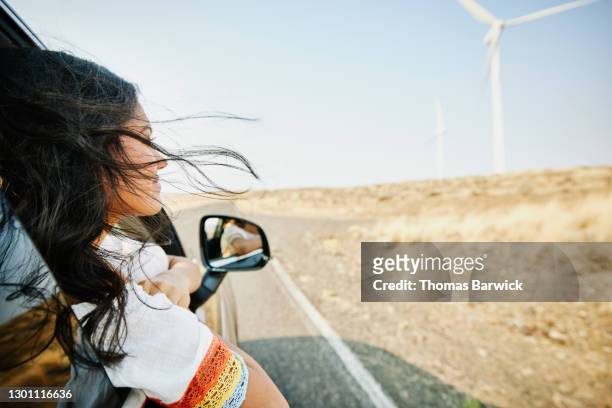 smiling teenage girl with head out car window and hair blowing in wind passing wind turbines in desert - light natural phenomenon foto e immagini stock