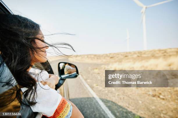 smiling teenage girl with head out car window and hair blowing in wind passing wind turbines in desert - car nature ストックフォトと画像