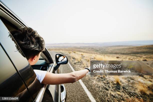 teenage boy with arm and head out car window during desert road trip - boy in wind stock-fotos und bilder