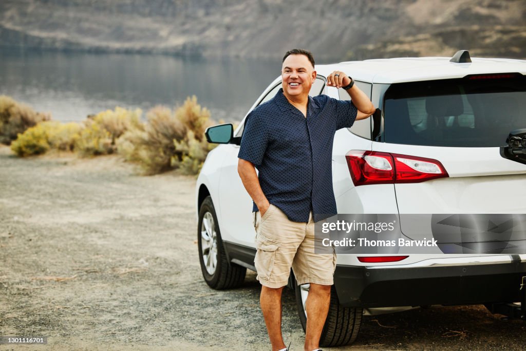 Smiling mature man standing next to car during road trip