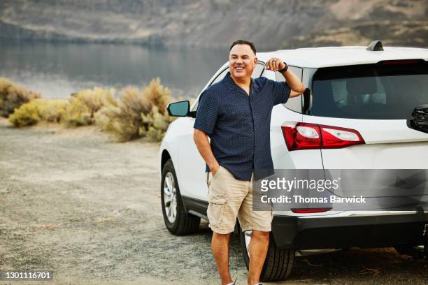 smiling mature man standing next to car during road trip - mens shorts stock pictures, royalty-free photos & images