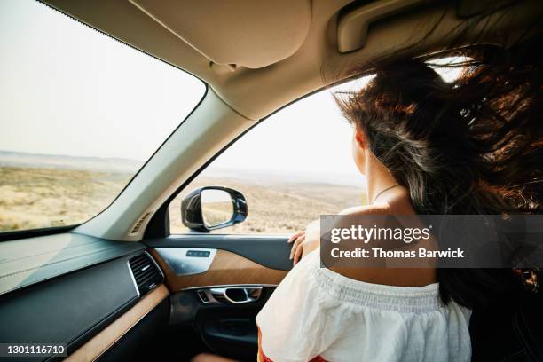 young woman looking out open window of car with hair blowing in wind - car top view photos et images de collection