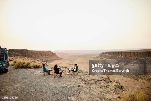Family relaxing in camp chairs near desert canyon during summer RV trip