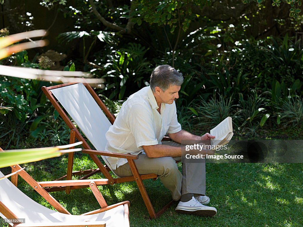 Man sitting on deckchair in garden reading book