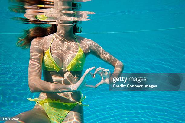 young woman making heart shape with hands underwater in swimming pool - swimming pool and hand stock-fotos und bilder