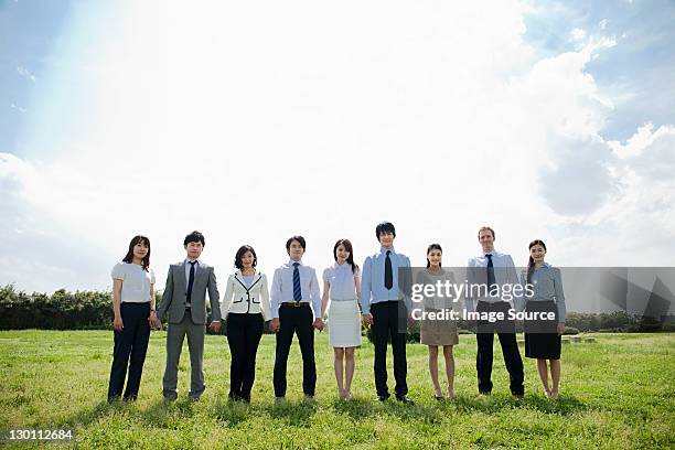 businesspeople in a row in field, holding hands - business people in a row stock pictures, royalty-free photos & images