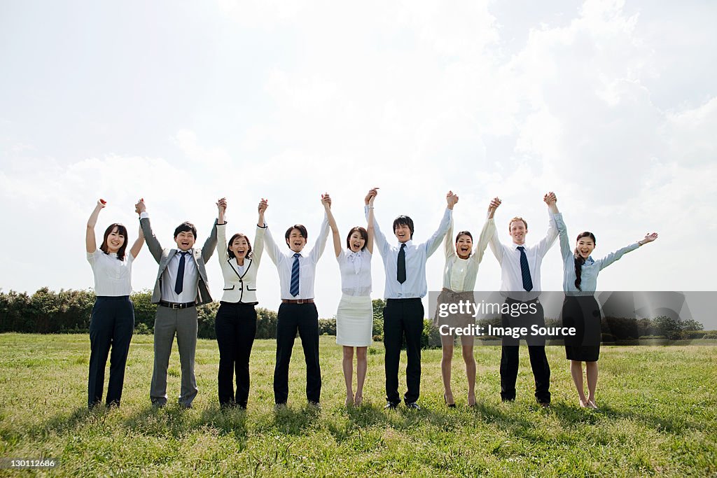 Businesspeople in a row in field, arms up