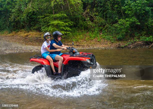 father and son driving quad bike in costa rica - car splashing water on people stock pictures, royalty-free photos & images