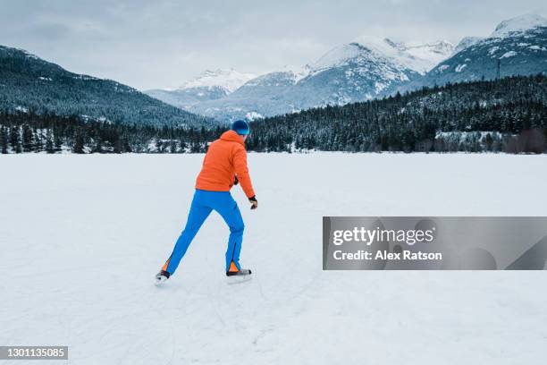 a man ice skates on green lake in whistler, bc with snowcapped mountains in the background - whistler mountain stock pictures, royalty-free photos & images