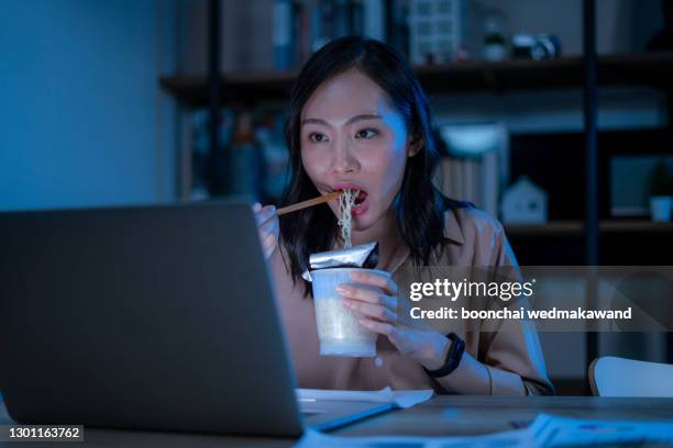asia freelance smart business women eating instant noodles while working on laptop in living room at home at night - eating ramen noodles stock pictures, royalty-free photos & images