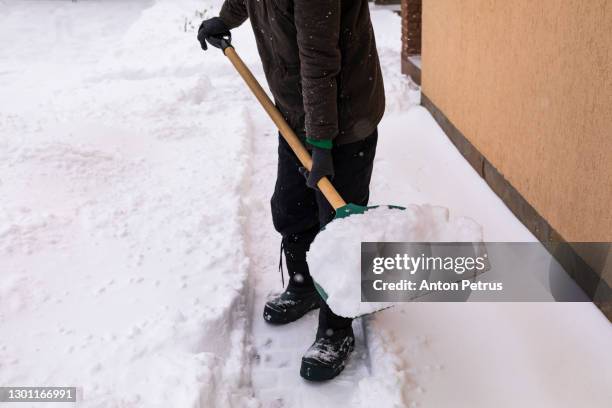 man with snow shovel cleans sidewalk - snow shovel stock-fotos und bilder