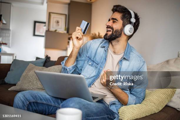 joven feliz sosteniendo una tarjeta de crédito y pagando en línea - compra por tarjeta de crédito fotografías e imágenes de stock