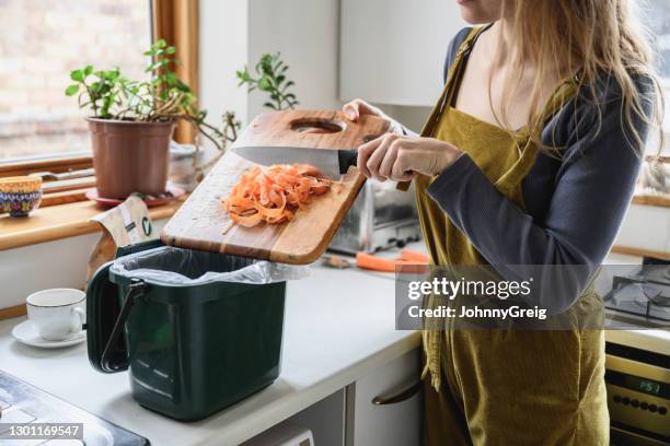 medio volwassen vrouw die wortelkrullen in compostbak zet - vuilnisbak stockfoto's en -beelden