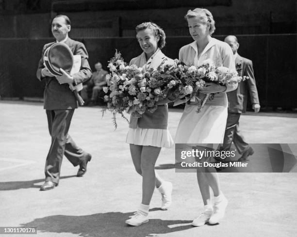 Maureen Connolly of the United States and compatriot Louise Brough walk on to Centre Court carrying bouquets of flowers before their Women's Singles...