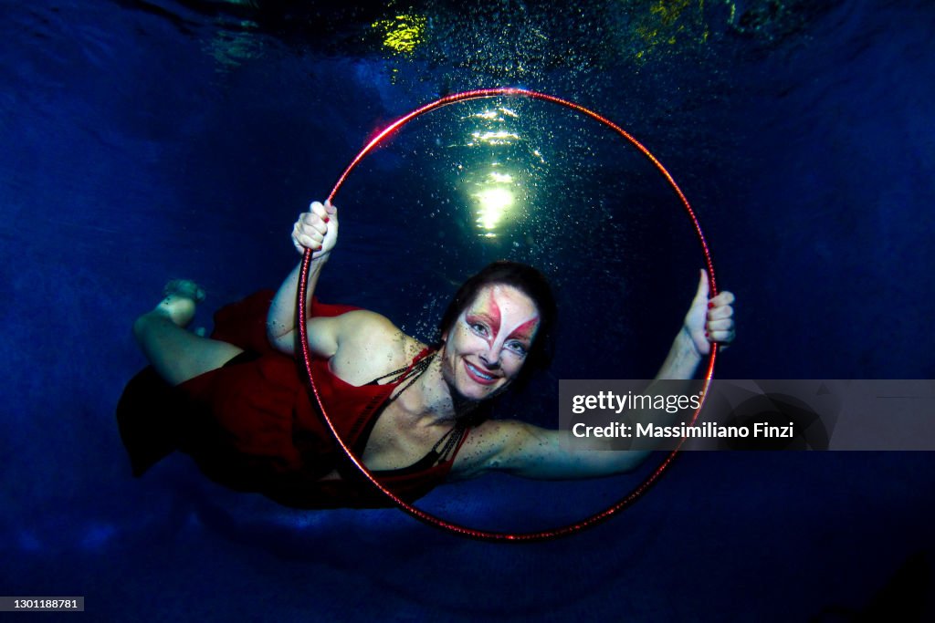 Underwater Circus. Model posing underwater in the pool with hula hoop dressed in red and strong make-up.