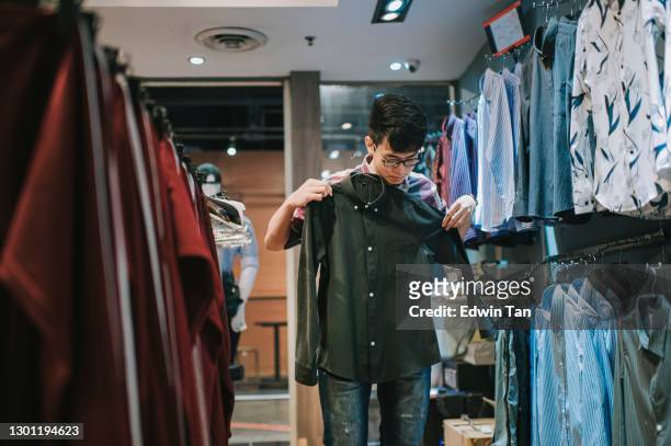 asiatico cinese maschio mano tenendo camicia uomo presso negozio di abbigliamento scegliendo quello giusto shopping - shopping male foto e immagini stock