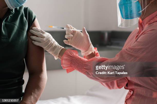 southeast asian female doctor giving vaccine shot on her male patient in a medical clinic - covid 19 vaccine stock pictures, royalty-free photos & images