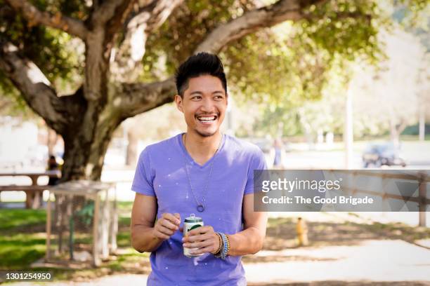 cheerful man holding beverage at park - purple shirt - fotografias e filmes do acervo