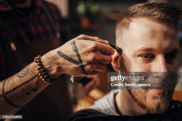 mannelijke kapper die bakkebaarden van cliënt in kapperswinkel snijdt - barbers stockfoto's en -beelden